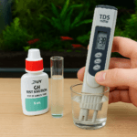 Water testing setup with digital TDS meter showing 138 ppm, GH test kit, and a shrimp tank in the background